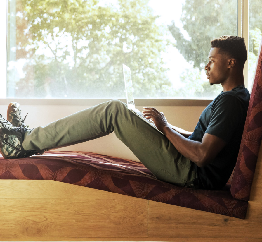 A guy on his computer, sitting by the window.